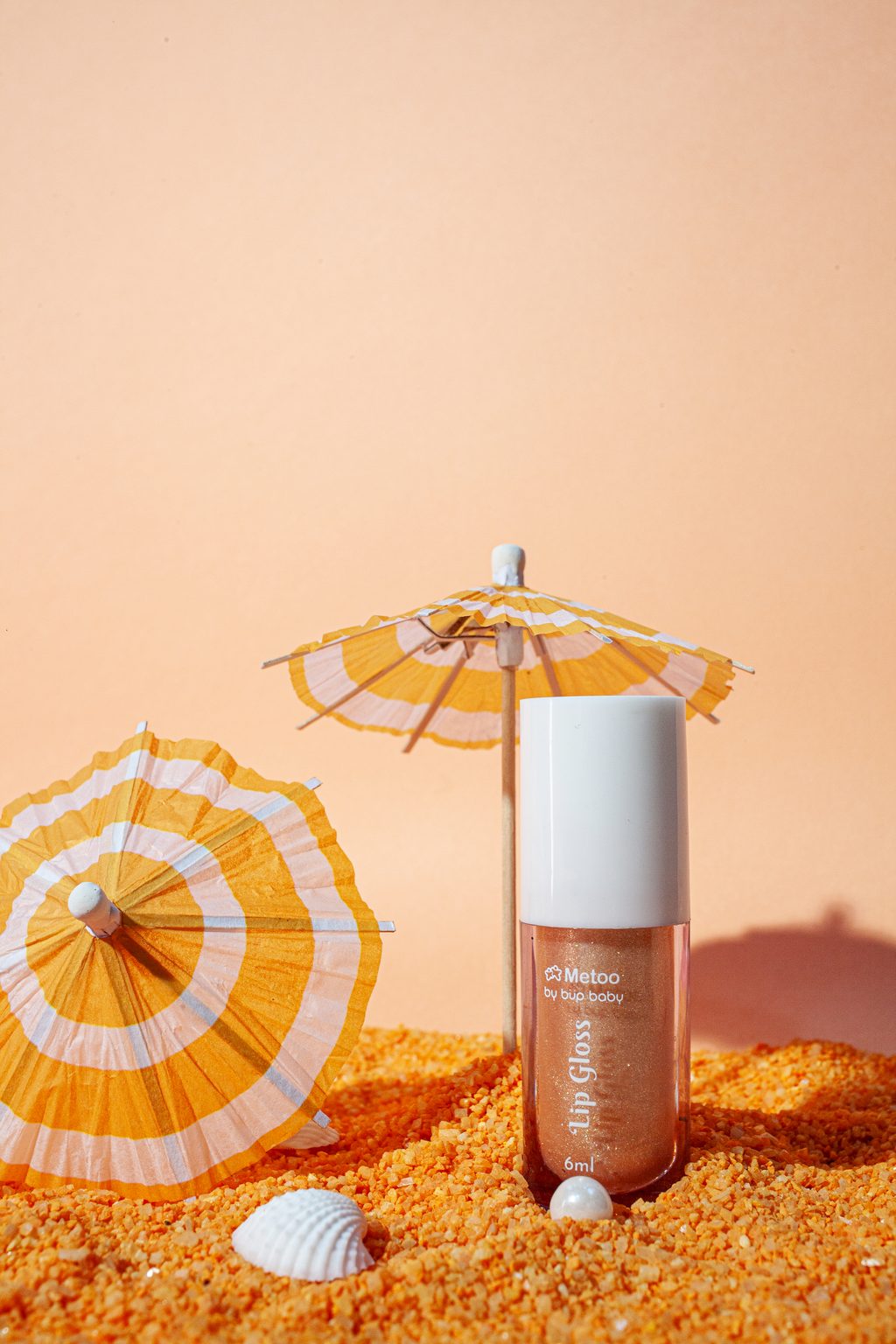 Frasco dourado do gloss Metoo na areia laranja, cor por sabor em fotografia de produto